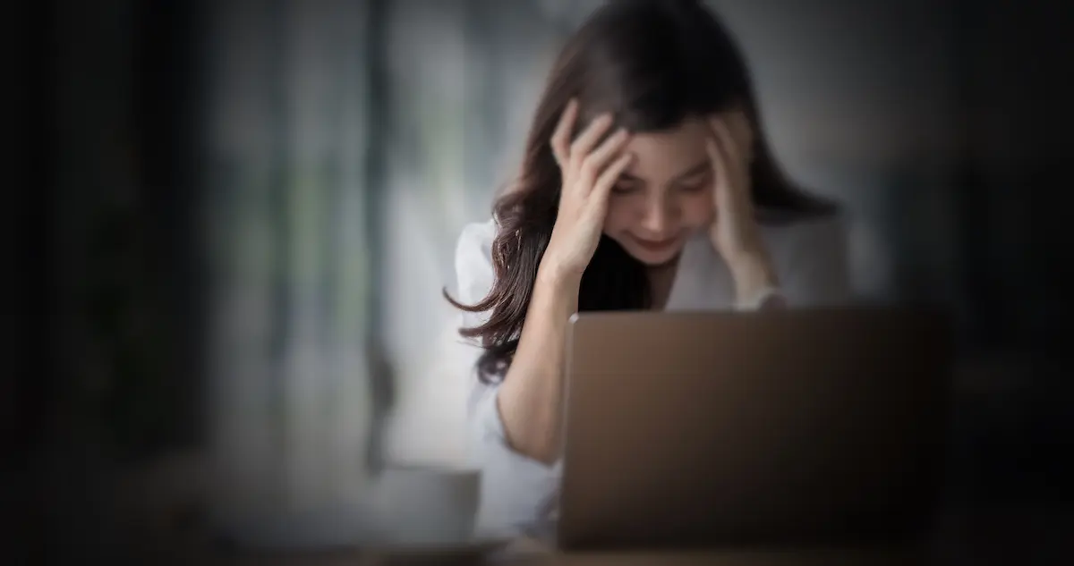 woman in front of a laptop with her head in her hands