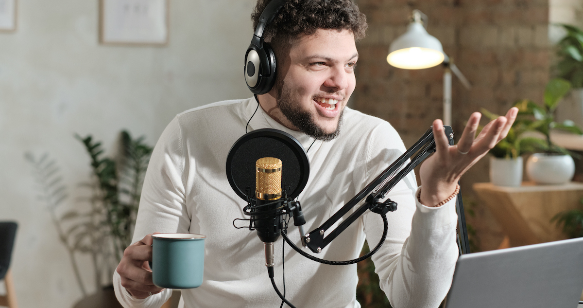 Podcast hosts: Young man in headphones using microphone and recording podcast.