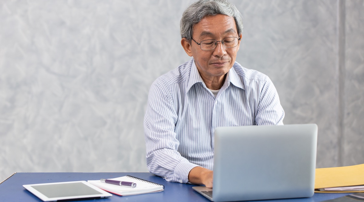 Work from home: senior man working at his desk in front of a laptop