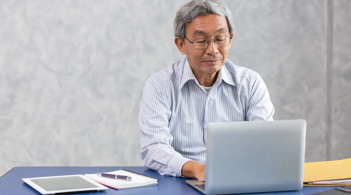 Work from home: senior man working at his desk in front of a laptop