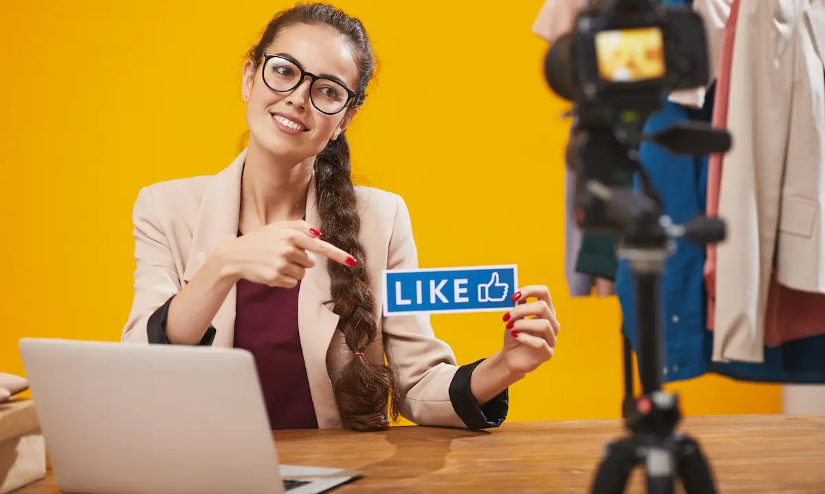 Influencers: image of a young female influencer holding a 'like' sign and pointing to it on camera