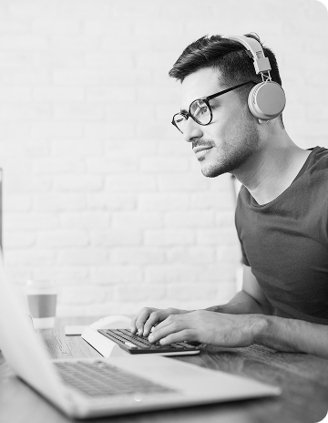 A male video producer listens to voice over samples on a laptop, looking to hire voice actors online. 